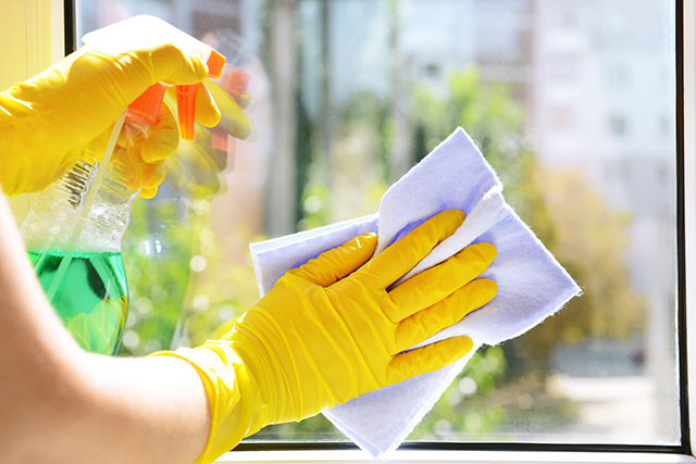 Person wearing yellow gloves cleaning a window with a spray bottle and cloth.