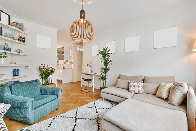 Modern living room with a teal armchair, beige sectional sofa, wooden floor, pendant light, and a small dining area in the background.